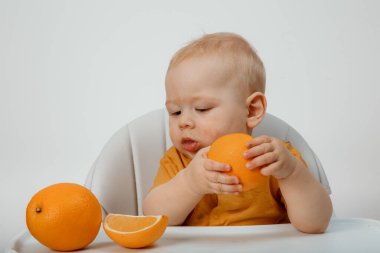A little boyin a t-shirt sitting in a childs chair eating an orange. Beautiful Baby boy eating an orange.