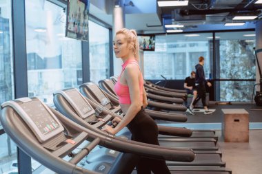 Koşu pistindeki iki çekici spor kadınının yan görünüşü. Çekici genç sporcu kadın spor salonunda çalışıyor. Koşu bandında koşuyor.