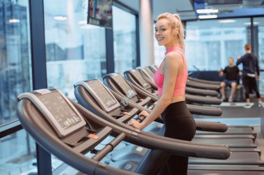 Koşu pistindeki iki çekici spor kadınının yan görünüşü. Çekici genç sporcu kadın spor salonunda çalışıyor. Koşu bandında koşuyor.