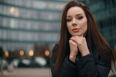 People lifestyle. Young stylish woman brunette near the office building. Glamorous young woman brunette in stylish clothes straightens hair.