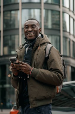 Genç Afro-Amerikalı şehirde akıllı telefon kullanıyor. Mutlu Afro-Amerikan adam şehir caddesinde cep telefonu kullanıyor. Açık havada yürümek, cep telefonu kullanmak. Navigatörde yön aranıyor.