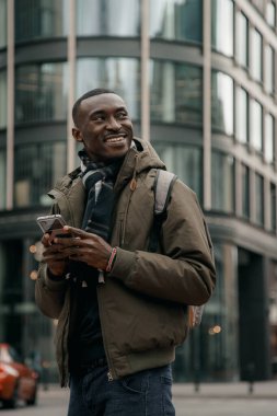 Genç Afro-Amerikalı şehirde akıllı telefon kullanıyor. Mutlu Afro-Amerikan adam şehir caddesinde cep telefonu kullanıyor. Açık havada yürümek, cep telefonu kullanmak. Navigatörde yön aranıyor.