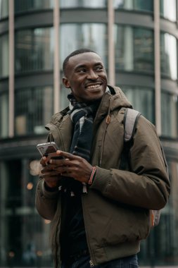 Genç Afro-Amerikalı şehirde akıllı telefon kullanıyor. Mutlu Afro-Amerikan adam şehir caddesinde cep telefonu kullanıyor. Açık havada yürümek, cep telefonu kullanmak. Navigatörde yön aranıyor.