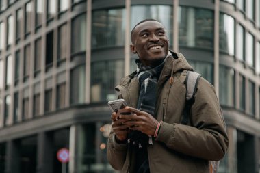 Genç Afro-Amerikalı şehirde akıllı telefon kullanıyor. Mutlu Afro-Amerikan adam şehir caddesinde cep telefonu kullanıyor. Açık havada yürümek, cep telefonu kullanmak. Navigatörde yön aranıyor.