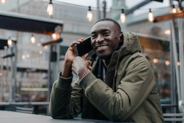 İş adamı Afro-Amerikan adam takım elbise giyer ve ofisinde oturur ve telefonda konuşur. Restoranda cep telefonuyla konuşan bir adam. Otururken cep telefonuyla konuşan gülümseyen adamın portresi.