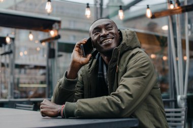 İş adamı Afro-Amerikan adam takım elbise giyer ve ofisinde oturur ve telefonda konuşur. Restoranda cep telefonuyla konuşan bir adam. Otururken cep telefonuyla konuşan gülümseyen adamın portresi.
