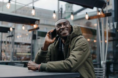 İş adamı Afro-Amerikan adam takım elbise giyer ve ofisinde oturur ve telefonda konuşur. Restoranda cep telefonuyla konuşan bir adam. Otururken cep telefonuyla konuşan gülümseyen adamın portresi.