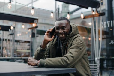 İş adamı Afro-Amerikan adam takım elbise giyer ve ofisinde oturur ve telefonda konuşur. Restoranda cep telefonuyla konuşan bir adam. Otururken cep telefonuyla konuşan gülümseyen adamın portresi.