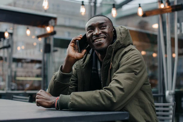 İş adamı Afro-Amerikan adam takım elbise giyer ve ofisinde oturur ve telefonda konuşur. Restoranda cep telefonuyla konuşan bir adam. Otururken cep telefonuyla konuşan gülümseyen adamın portresi.