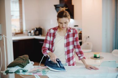 Genç ve güzel bir kadın temiz çamaşırları içeride ütülüyor. Giysileri ütüleyen genç bir kadın. Kar beyazı gömlek.