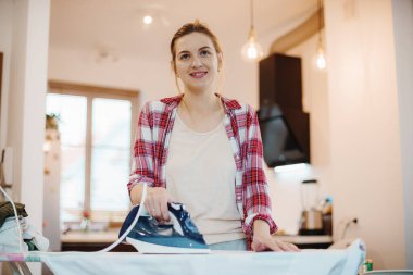 Genç ve güzel bir kadın temiz çamaşırları içeride ütülüyor. Giysileri ütüleyen genç bir kadın. Kar beyazı gömlek.
