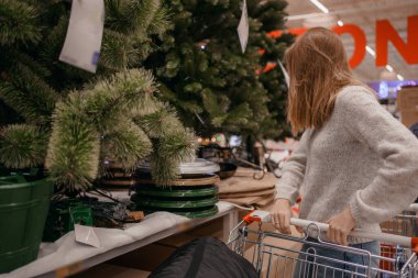 Xmas mağazasında yapay Noel ağacı seçen sevimli genç bir kadın. Noel konsept mağazasında inanılmaz Avrupalı. Bir kadın mağazadan yılbaşı ağacı için süslemeler alıyor..