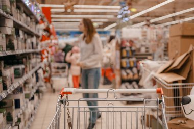 Süpermarkette sepeti olan güzel bir kadın. Süpermarkette Mutlu Kadın Alışverişi. Müşteri markette alışveriş arabasını itiyor, eller kapalı..