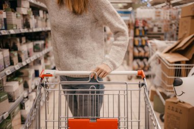 Süpermarkette sepeti olan güzel bir kadın. Süpermarkette Mutlu Kadın Alışverişi. Müşteri markette alışveriş arabasını itiyor, eller kapalı..