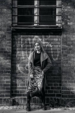 Stylish blond woman posing near red brick wall. Beautiful fashionable girl stands near the brick wall. Fashionable woman in spectacles hanging out in night city. Travel Europe.
