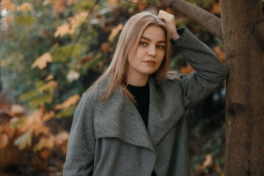 Güzel kız güz gününde poz veriyor, güzel havanın tadını çıkarıyor. Sonbahar yapraklı genç bir kadın. Kürsüde oturan genç ve güzel sarışın kadının portresi. Sonbahar Parkı.