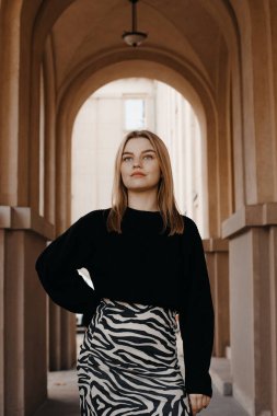 Eski şehirde, sıcak bir sonbahar gününde kemer yolunda poz veren güzel bir kız. Güzel binanın dışında sarışın bir kadın. Eski binalar ve duvarlar. Kemer ve sütunlu koridor.