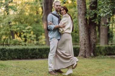 Romantizm, kaynaşma ve yaz tatili için parkta çiftlerle aşk, sarılma ve mutluluk. Doğada birbirine sarılıp gülümseyen sevimli genç bir çift..