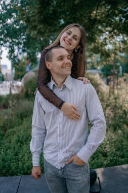 Aşık mutlu çift şehir parkında eğleniyor. Bir bankta oturan genç bir adam kız arkadaşını kollarında tutarken birbirlerine gülümsüyorlar. Şehir doğası, romantizm.