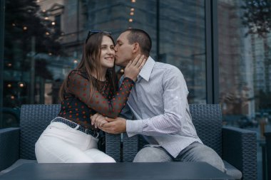Kafenin dışındaki masada oturan bir çift aşığın romantik sahnesi. Erkek ve kadın nazikçe öpüşüyor, el ele tutuşuyorlar, bu da yakınlıklarını vurguluyor..
