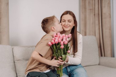 Bir anne ve oğlu arasında, ona bir buket pembe lale hediye ederken çok güzel bir an. Anneler Günü ve bahar kutlamaları için mükemmel sevgi, minnettarlık ve aile bağlarının güzel bir sahnesi..