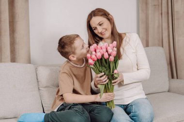Bir anne ve oğlu arasında, ona bir buket pembe lale hediye ederken çok güzel bir an. Anneler Günü ve bahar kutlamaları için mükemmel sevgi, minnettarlık ve aile bağlarının güzel bir sahnesi..
