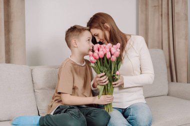 Bir anne ve oğlu arasında, ona bir buket pembe lale hediye ederken çok güzel bir an. Anneler Günü ve bahar kutlamaları için mükemmel sevgi, minnettarlık ve aile bağlarının güzel bir sahnesi..