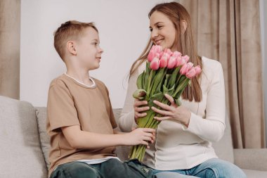 Bir anne ve oğlu arasında, ona bir buket pembe lale hediye ederken çok güzel bir an. Anneler Günü ve bahar kutlamaları için mükemmel sevgi, minnettarlık ve aile bağlarının güzel bir sahnesi..