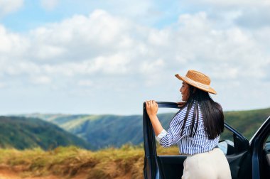 Uzak bir yolda arabada duran mutlu bir İspanyol kadının arka görüntüsü.