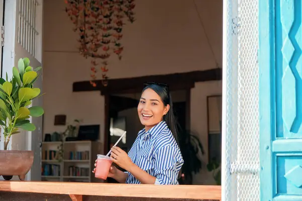 Elinde pipetle pembe bir içecek tutan mutlu bir genç kadın. Arka plandaki dekorasyonlar