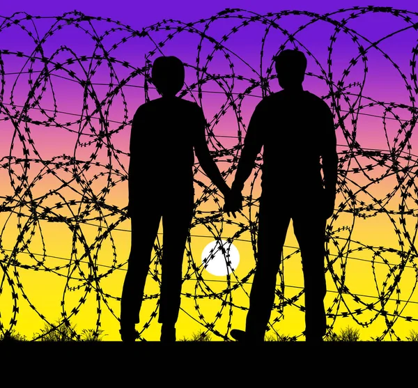 A couple hold hands and watch the sunset through a razor wire fence at the USA and Mexico border. They cannot cross, only look through the razor wire to see the USA.