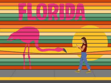 Telefondaki bir kız Florida turizmi için çok renkli bir reklam panosunun önünden geçiyor. 3 boyutlu resimde bir flamingo ve gün batımı yer alıyor.