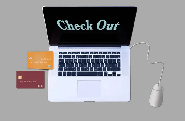 Two credit cards are seen next to a laptop computer with the words check out on the screen in a 3-d illustration about using a credit card online for purchases.