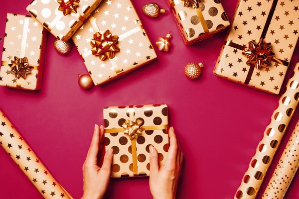 女人的手拿着礼品盒 上面有金色的星形蝴蝶结和红色背景的缎带 包装礼物的概念 圣诞节的背景顶部视图 2023年色彩趋势年 — 图库照片