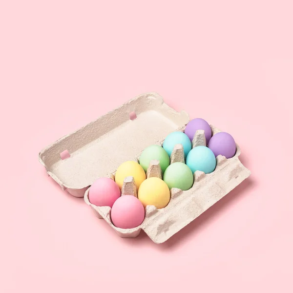 Pastel colored Easter Eggs in egg box on pink background. Rainbow, minimal style. Easter greeting card.