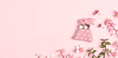 Paskalya bayrağınız kutlu olsun. Paskalya süsleri, tavşancık, pembe arka planda çimenler ve çiçekler. Uzayı kopyala, düz yat.