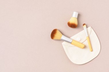 Bej arka planda bambu kozmetik fırçalar ve pamuk torbaları. Doğal, çevre dostu makyaj aletleri. Boşluğu kopyala.