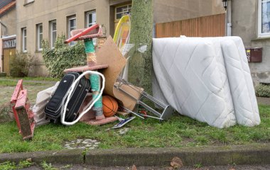 Yastıklı, ütü tahtası ve kırmızı merdivenli büyük bir çöp yığını.