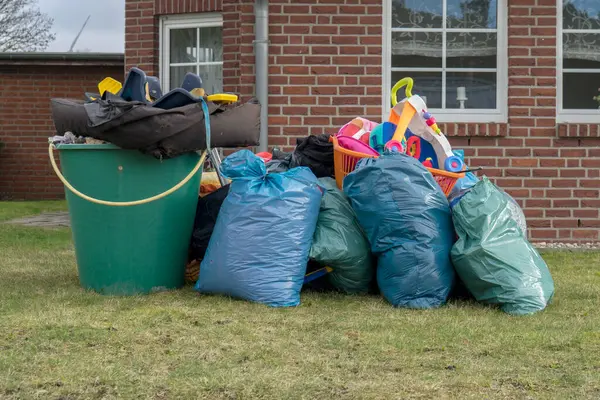 Pile of bulky waste in front of a house with garbage bags, rain barrels and toy