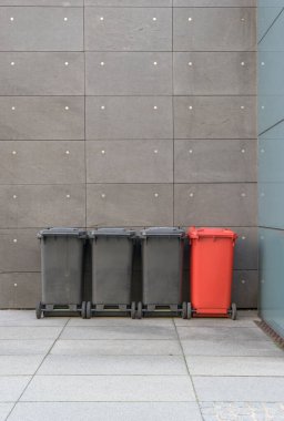 Gri bir cephenin önünde siyah ve kırmızı çöp tenekeleri