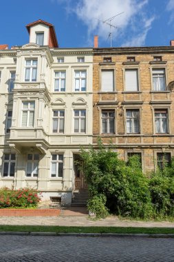 A renovated and a dilapidated terraced house with several floors and a front garden clipart