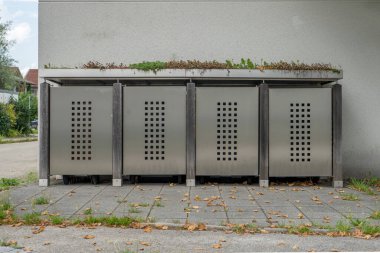 Estetik çöp tenekesi, metal kapılar, ahşap ve bitkiler bir evin önünde. 