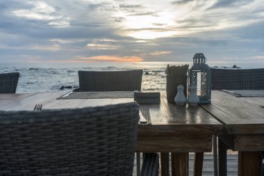 Akşam gökyüzü olan deniz kenarındaki masa ve sandalyelere yakın çekim