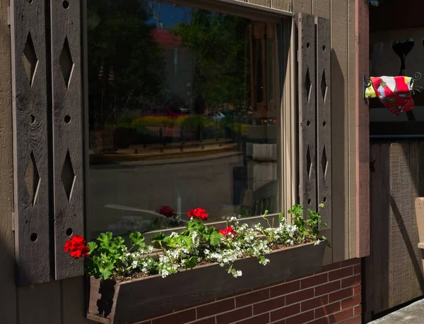 Traditional window box with geraniums below a large window reflecting the local scene in Sugarcreek, Ohio
