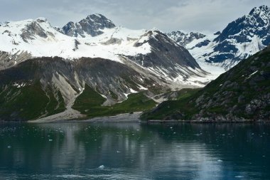 Alaska 'daki Buzul Körfezi Ulusal Parkı' nda buzla kaplı sakin sular üzerinde engebeli, karlı tepeler.