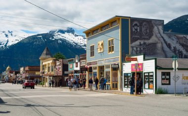 Skagway, AK, ABD - 25 Haziran 2024: Kar örtülü dağların zeminine kurulmuş klasik mağazaları ve turistik mekanlarıyla Broadway 'in aşağısına bakıyor.