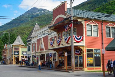 Skagway, AK, ABD - 25 Haziran 2024: Skagway 'de Broadway Caddesi' nde antika görünümlü hediyelik eşya dükkanları kuyruğu, orman dağlarının arkasında ve üzerinde yükselen.