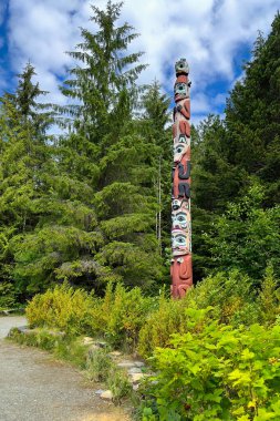 Saxman, AK, ABD - 27 Haziran 2024: Ketchikan, Alaska yakınlarındaki Saksonya Totem Parkı 'ndaki ağaçların arasında bir totem direği duruyor. Totemlerin sembolik temsillerinde atalarının ve mirasının izini sürdükleri düşünülür..