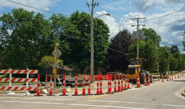 Twinsburg, OH, USA - July 18, 2024: Road construction vehicles and other materials sit behind a barrier of traffic cones on a city street during a water main replacement. clipart