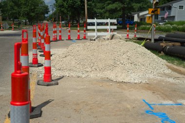 Traffic cones, a gravel pile, and pipe sections mark the start of a water main replacement project. clipart